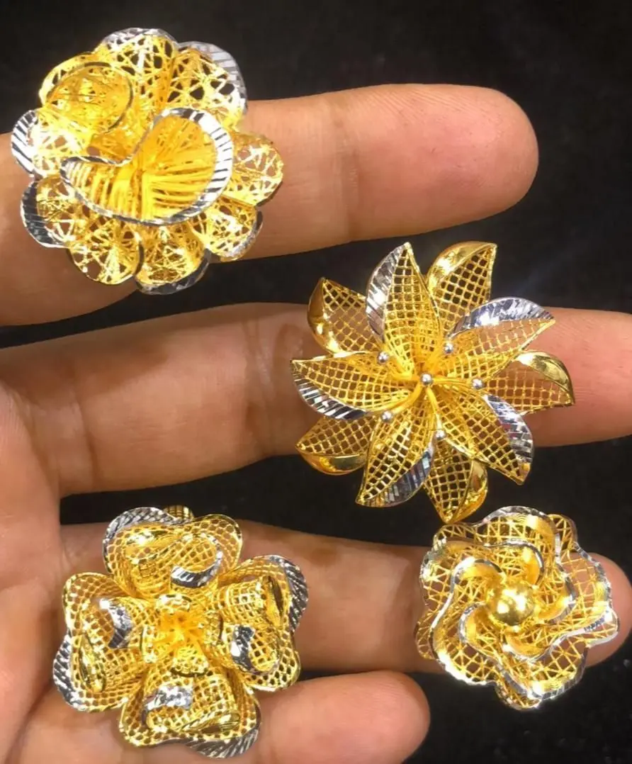 A hand holding four two-tone filigree floral pieces in gold and white metal.