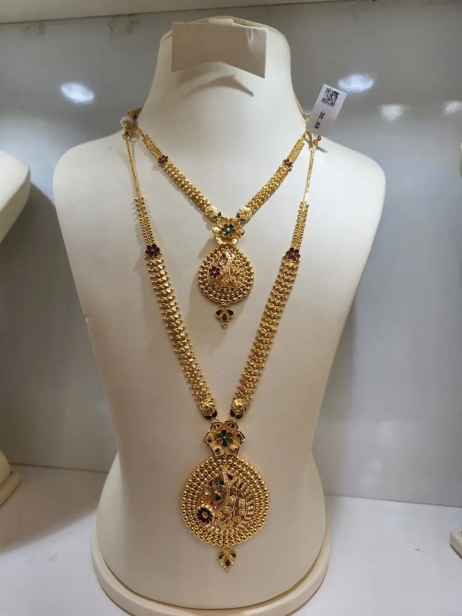 A two-layer bridal set on a display bust: a short necklace and a long haram with ruby and emerald stones.