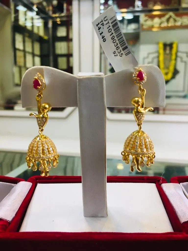 A pair of gold jhumka earrings on a grey display stand.