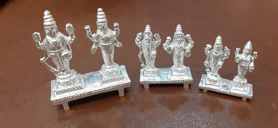 Three silver deity idols standing on a wooden counter.